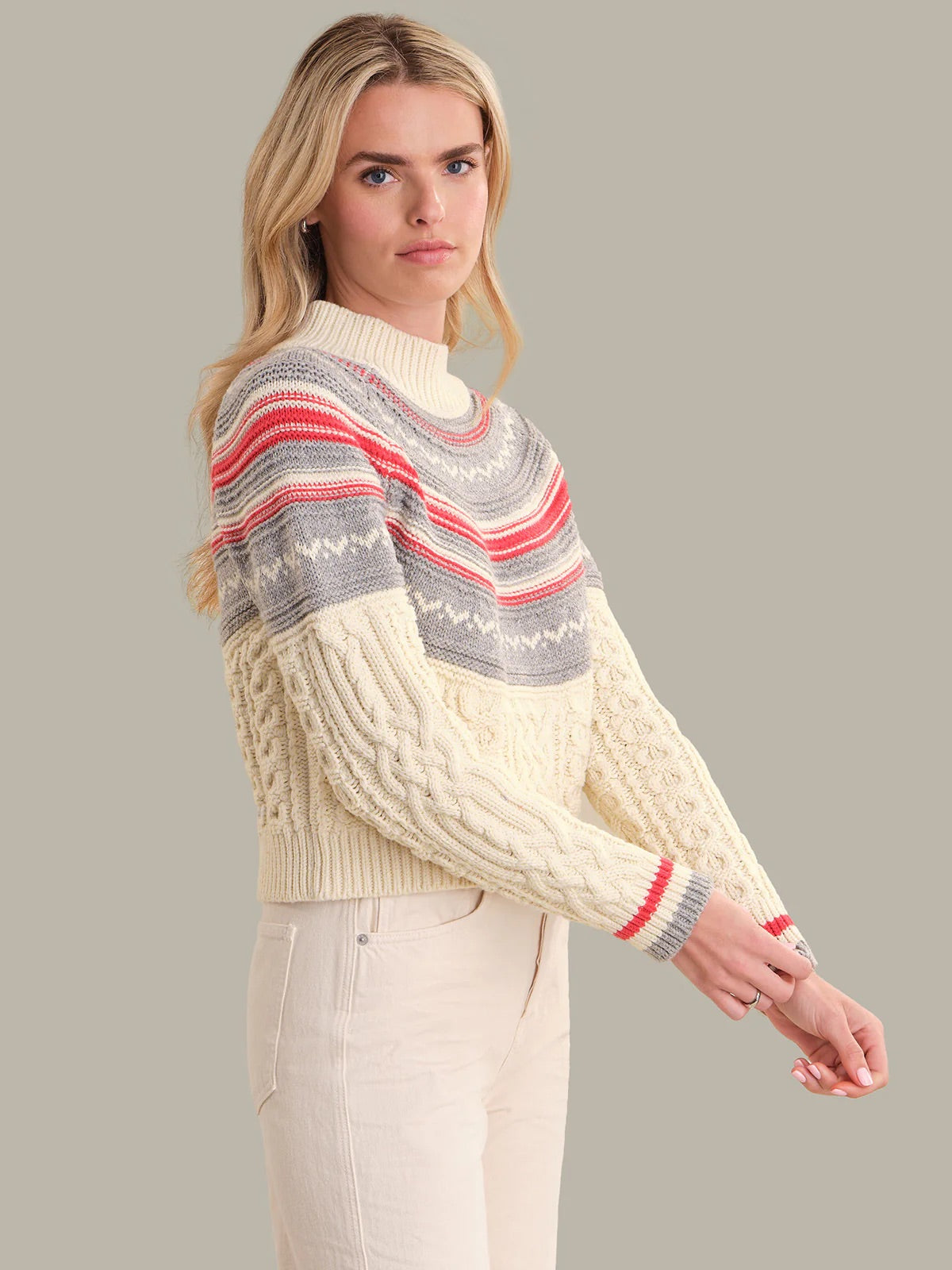 Woman wearing a cream sweater with colorful stripes on a gray background