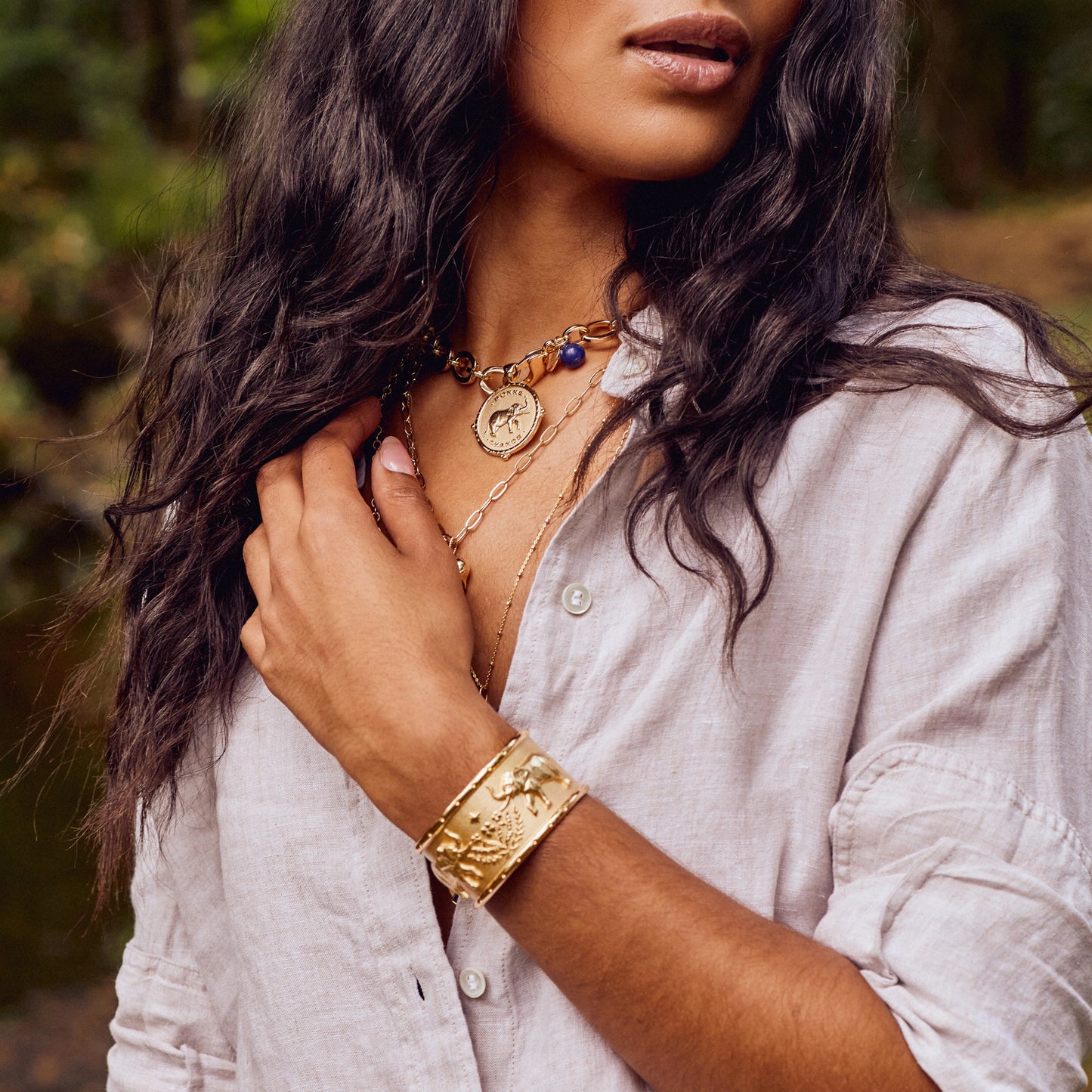Woman wearing gold jewelry outdoors with a blurred natural background