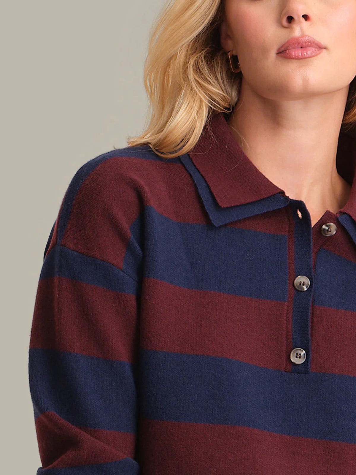 Close-up of a person wearing a maroon and navy striped sweater with a neutral background
