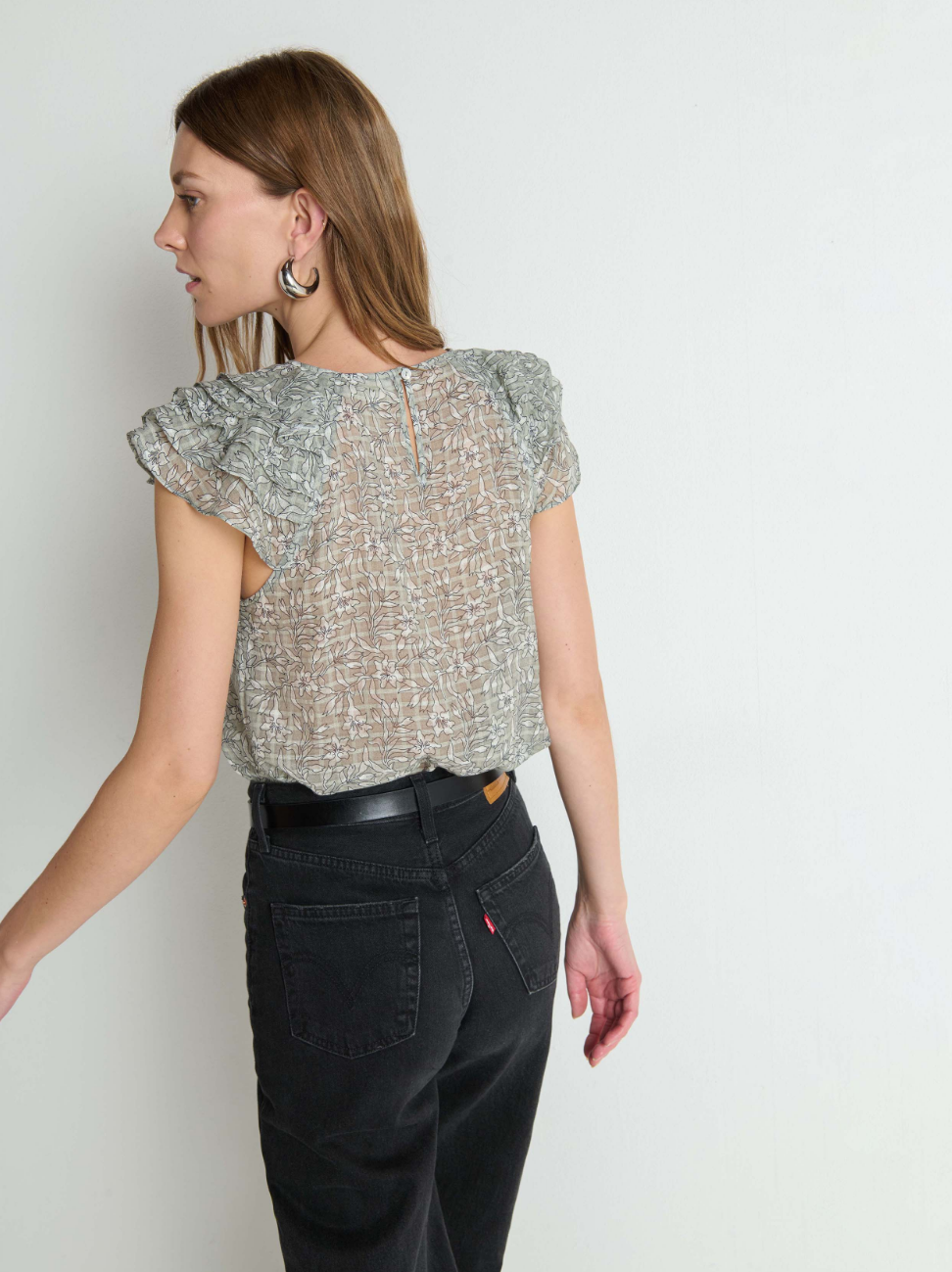 Woman wearing a patterned top and black pants against a white background