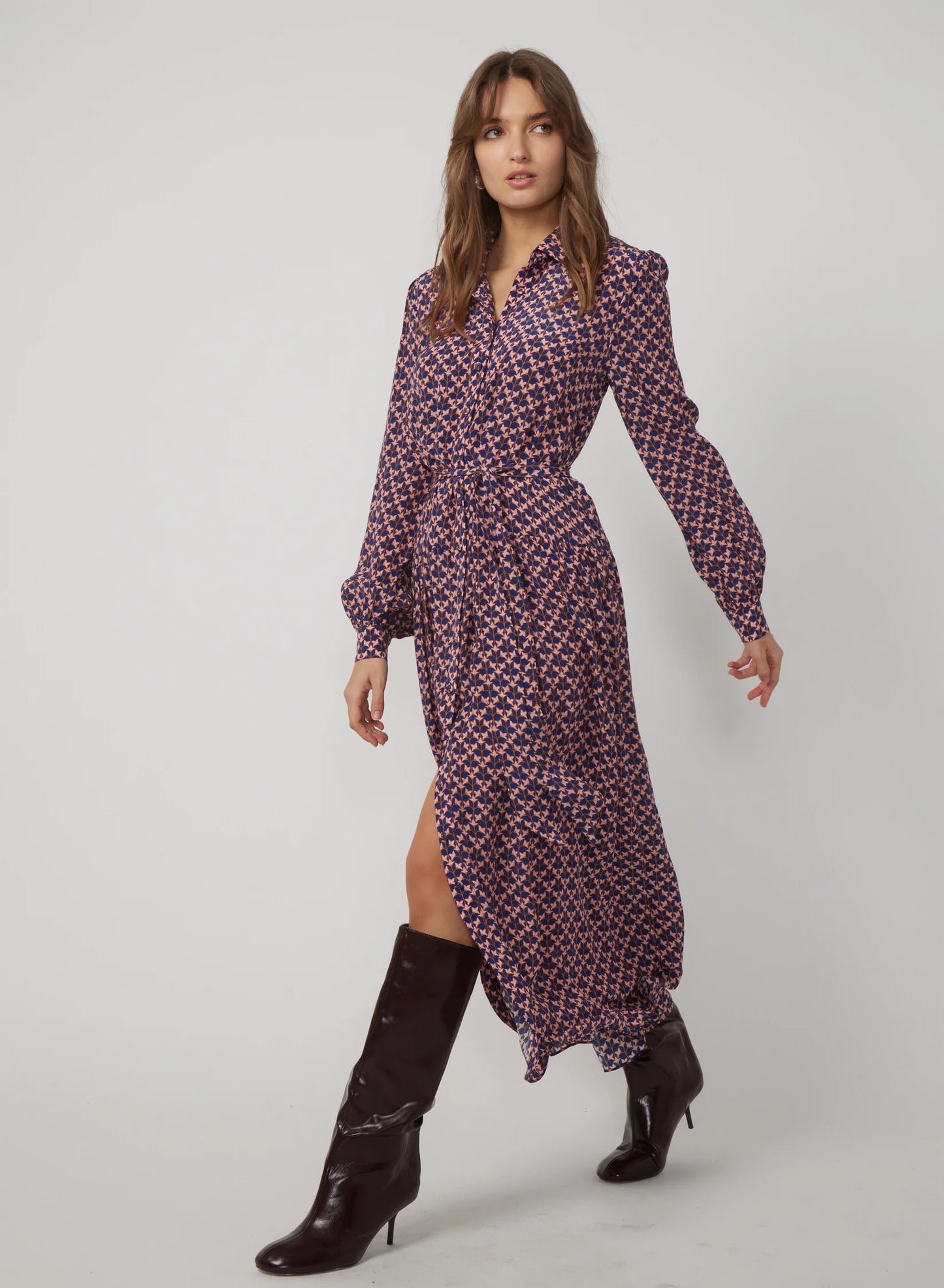 Woman wearing a patterned dress with a slit and black boots on a white background