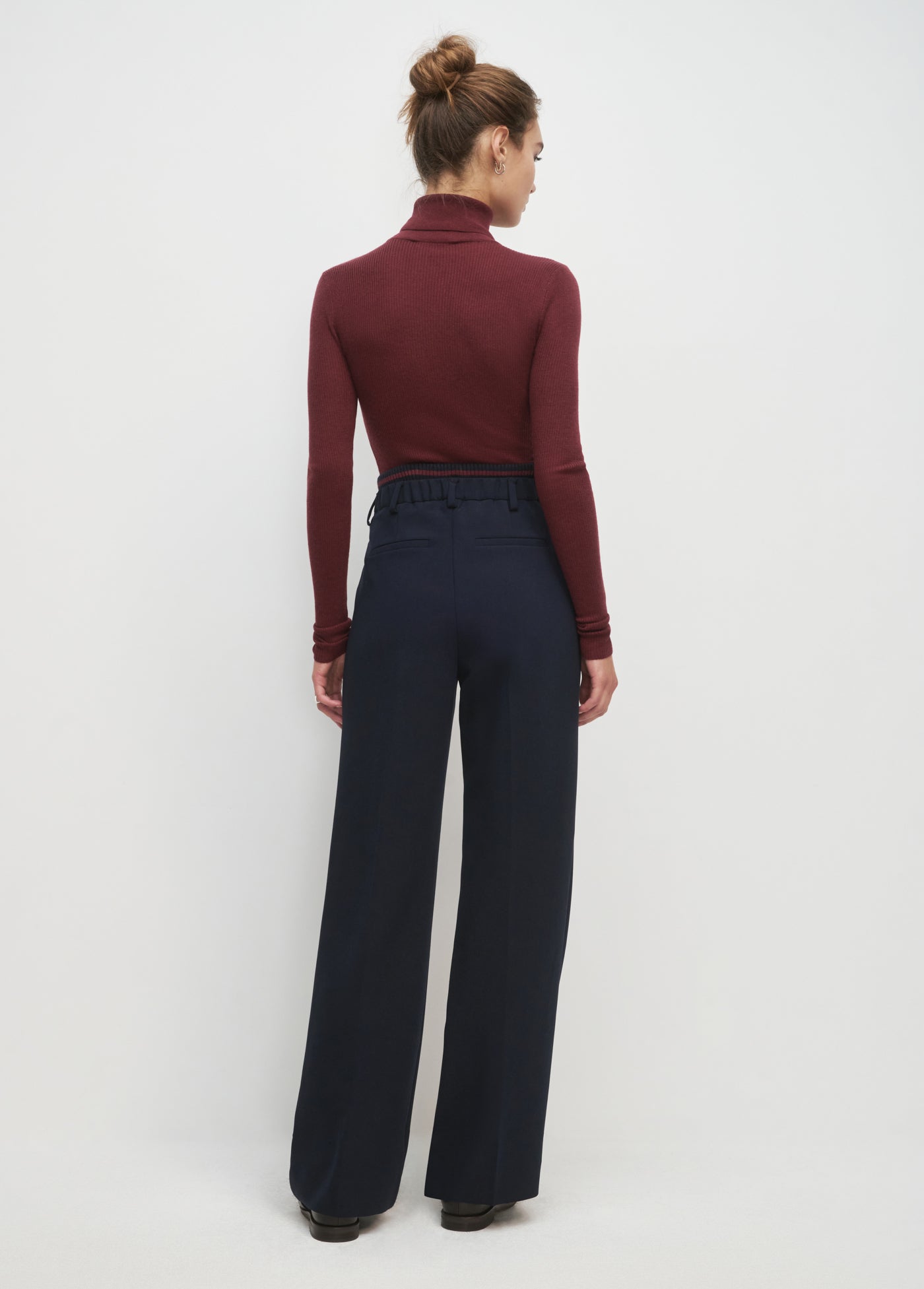 Woman wearing a burgundy turtleneck and navy high-waisted pants on a white background