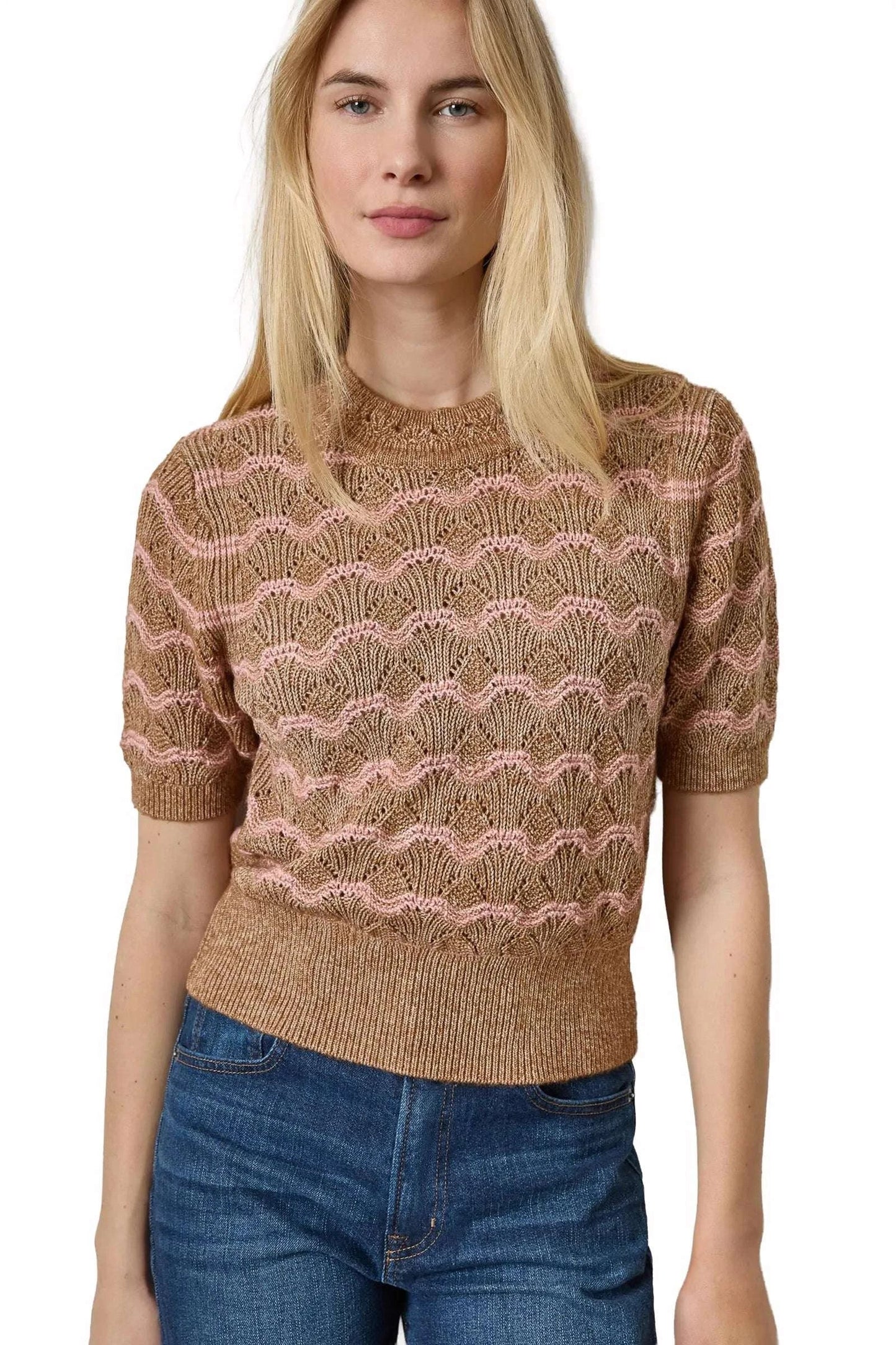 A woman wearing a short-sleeve knit sweater with a wavy, scallop-like pattern in brown and dusty pink, paired with blue jeans, against a plain white background.