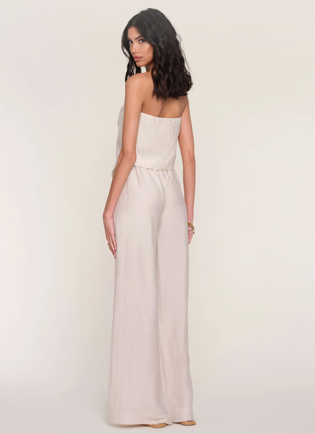 Woman wearing a strapless beige jumpsuit on a plain background