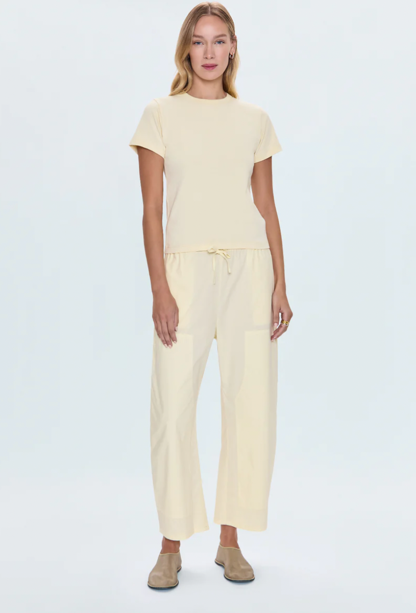 A female model wearing a beige Alba top and matching pants, with short sleeves and a round neckline.