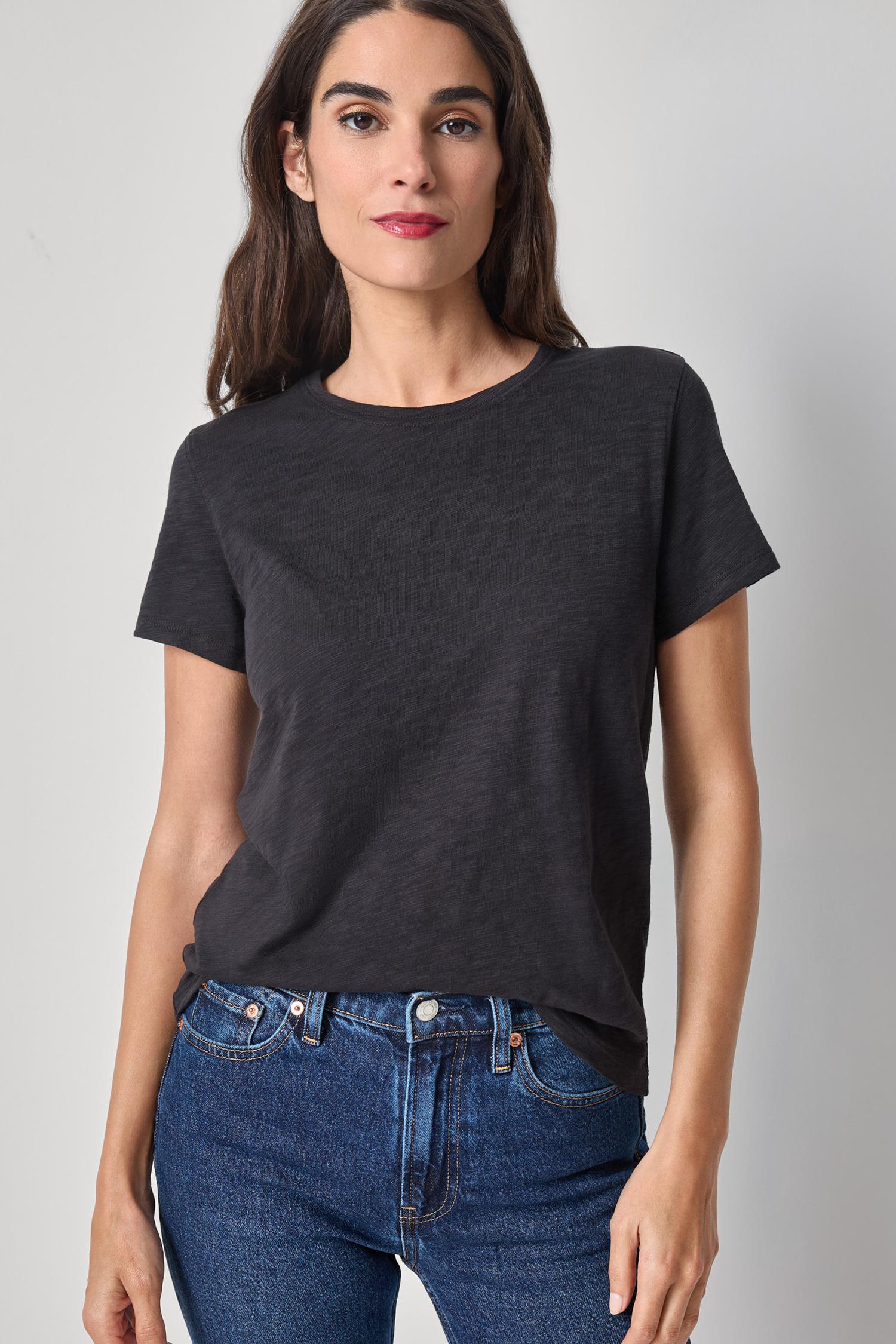 Woman wearing a black t-shirt and blue jeans against a gray background