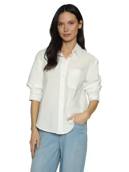 A woman modeling a white long-sleeve button-up shirt with a chest pocket, paired with light blue jeans, against a plain white background.