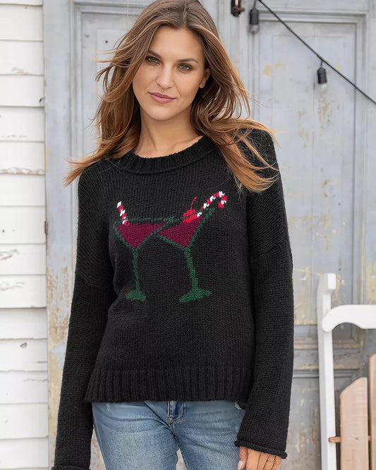 Woman wearing a black sweater with a festive design, standing in front of a rustic wooden door.