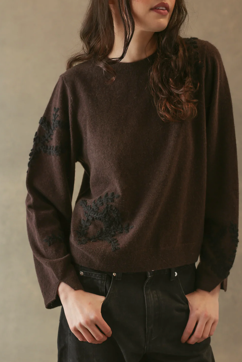 Person wearing a brown sweater with black embroidery on a beige background