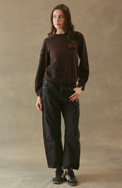 Person wearing a brown sweater and black pants against a beige background