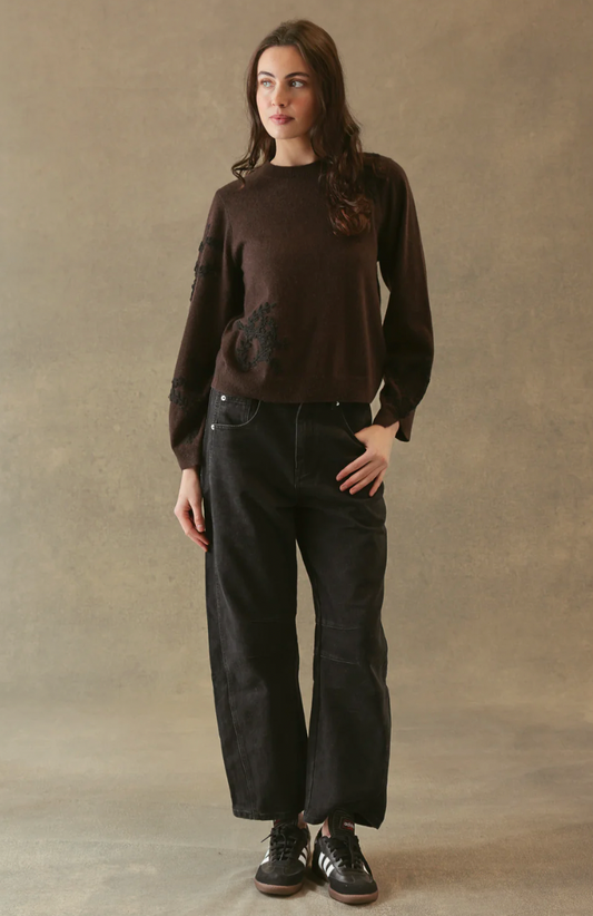 Person wearing a brown sweater and black pants against a beige background