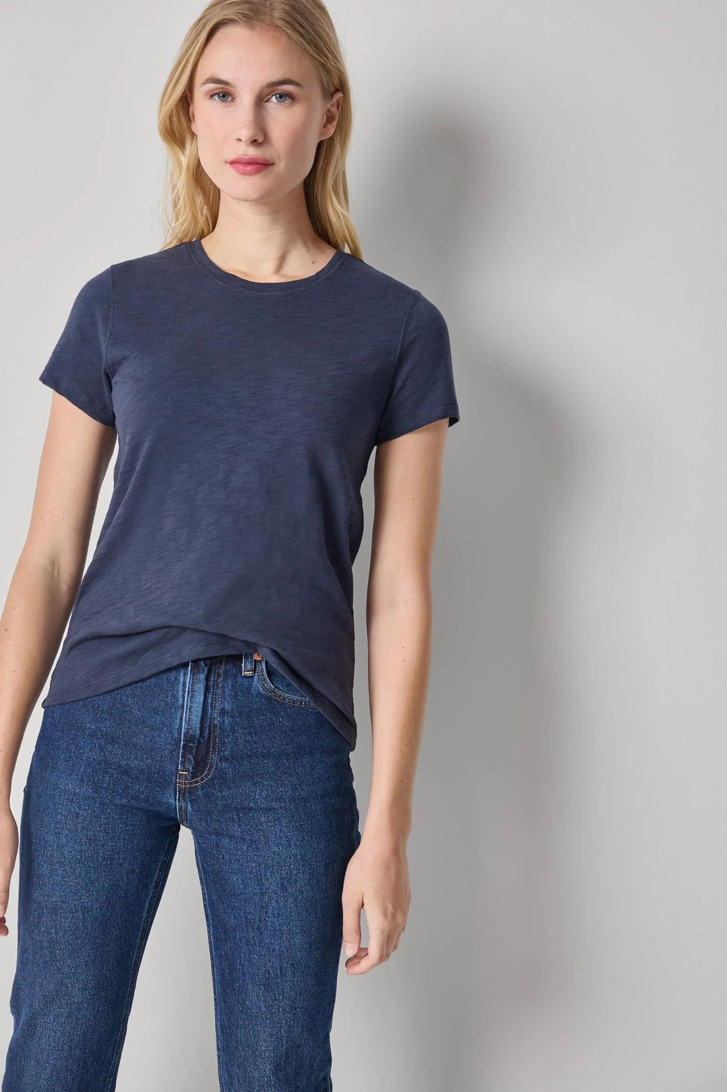 Woman wearing a navy blue t-shirt and jeans against a gray background