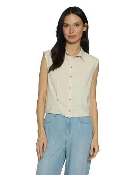 Woman wearing a beige sleeveless shirt and light blue jeans on a white background