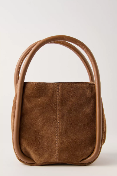 A brown suede handbag with a unique double-loop top handle, photographed against a plain light gray background.