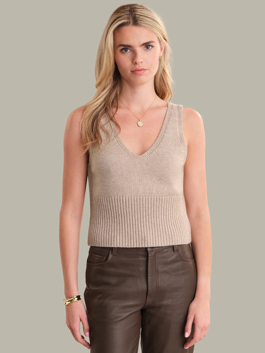Woman wearing a beige knit tank top and brown pants against a neutral background