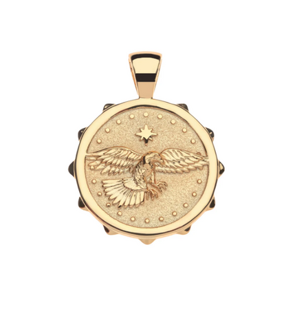 A round gold pendant featuring an embossed eagle design with outstretched wings, a star motif, and a textured center, suspended from a matching gold bail against a plain white background.