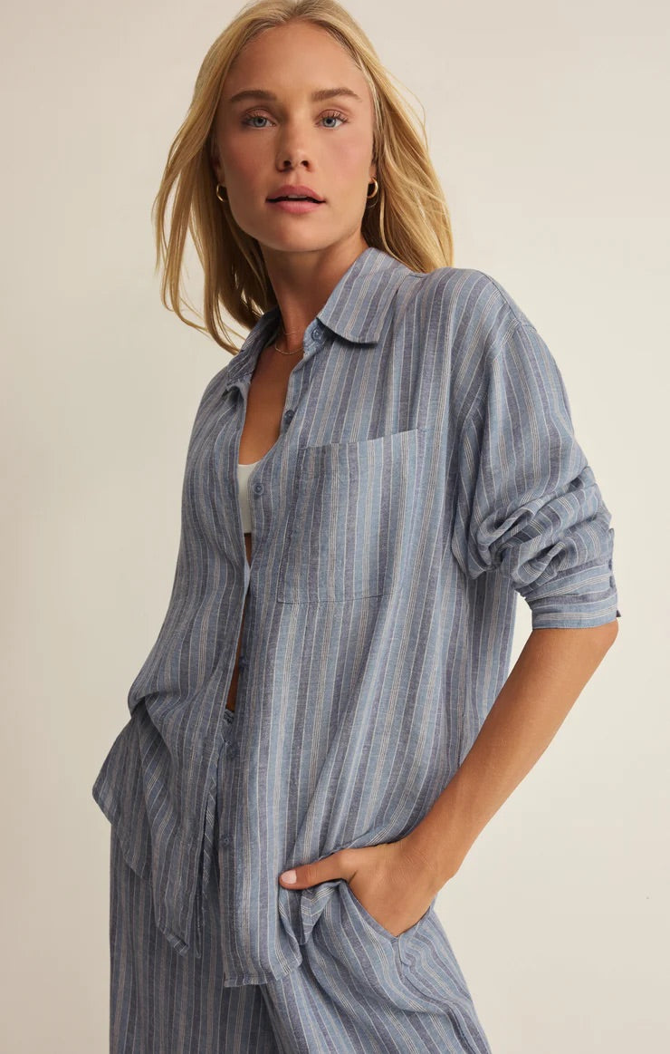 Woman wearing a blue striped shirt and pants against a beige background