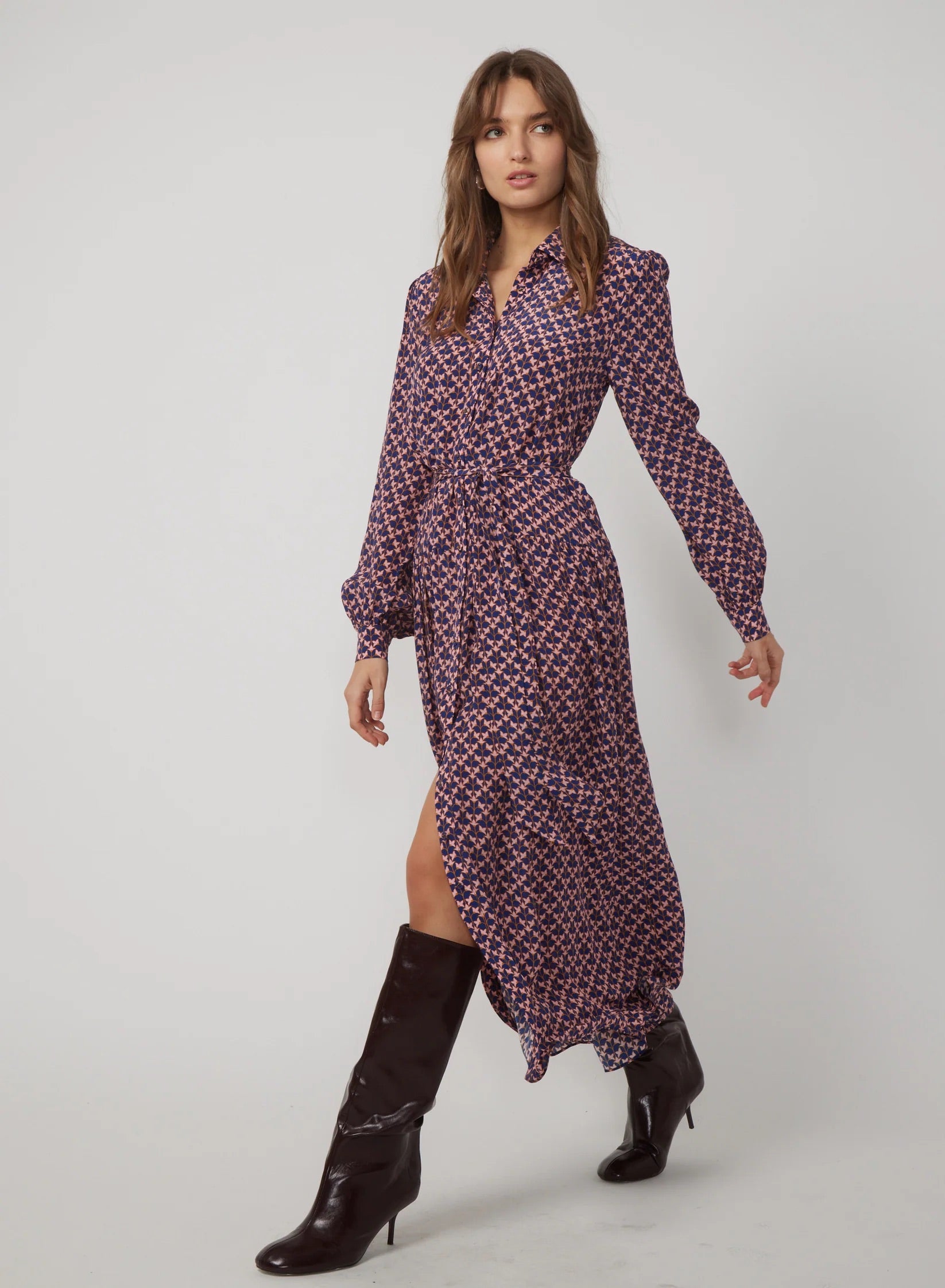 Woman wearing a patterned dress with a slit and black boots on a white background