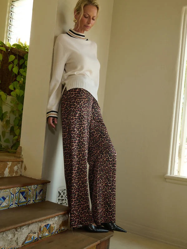 Woman in a white sweater and leopard print pants standing on a staircase.