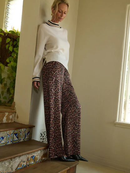 Woman in a white sweater and leopard print pants standing on a staircase.