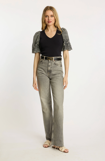 Woman wearing a black top with patterned sleeves and gray jeans on a white background