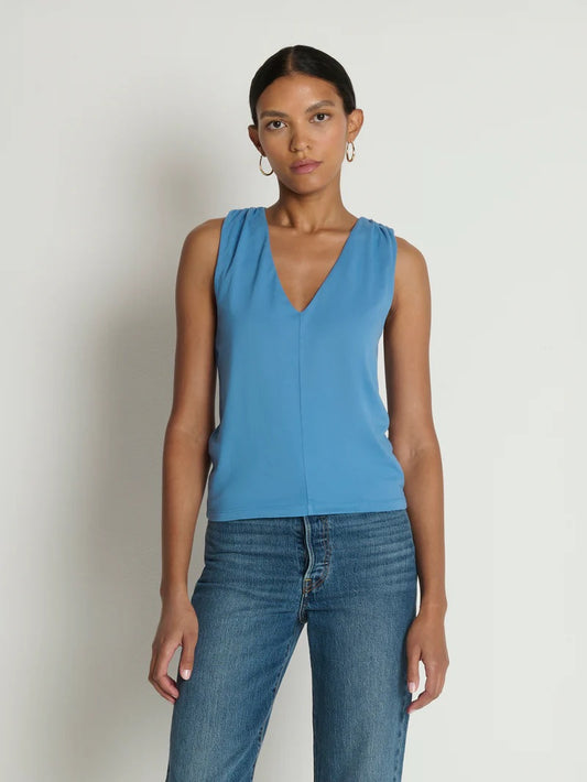 Woman wearing a blue sleeveless top and jeans against a plain background
