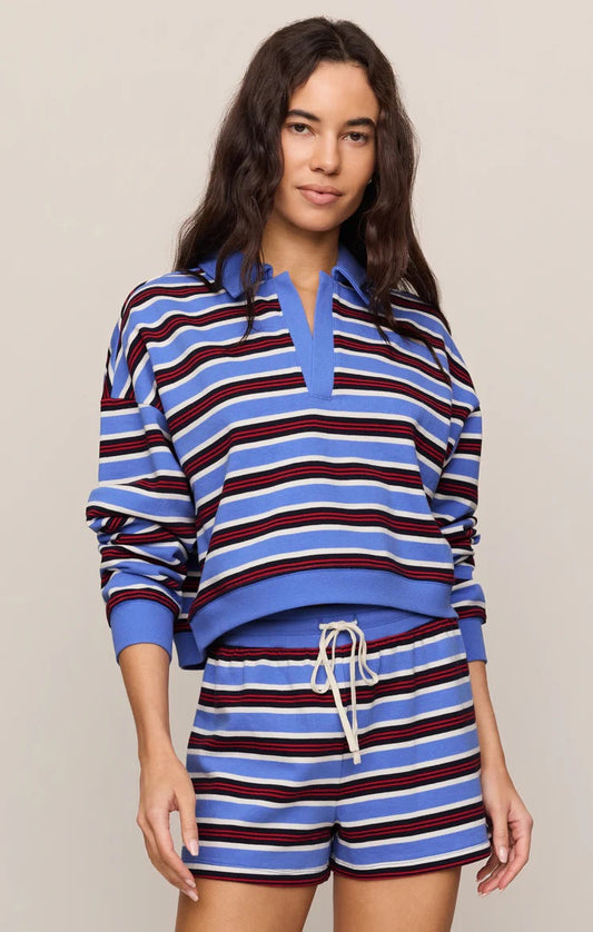 A woman modeling a matching two-piece lounge set with blue, white, and burgundy horizontal stripes. The set includes a long-sleeve half-placket top with a blue collar and matching striped shorts with a white drawstring.