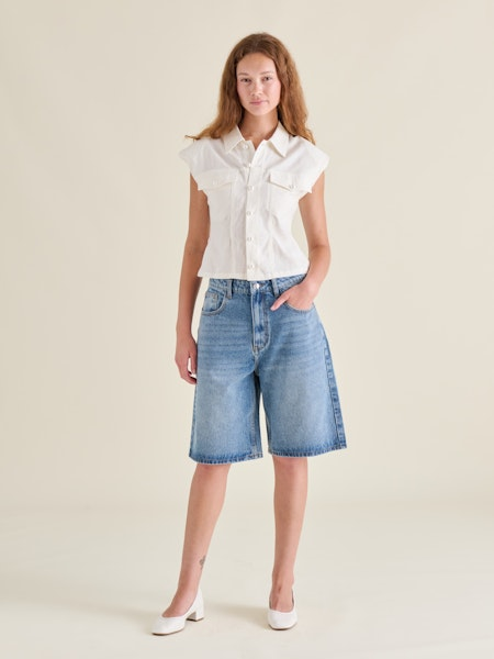 Woman wearing a white blouse and denim shorts on a plain background