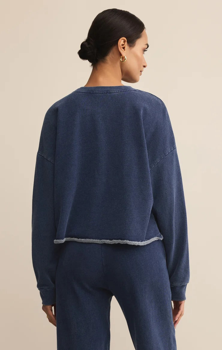 WOMEN IN BLUE SWEATSHIRT STANDING IN FRONT OF WHITE BACKGROUND