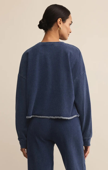 WOMEN IN BLUE SWEATSHIRT STANDING IN FRONT OF WHITE BACKGROUND
