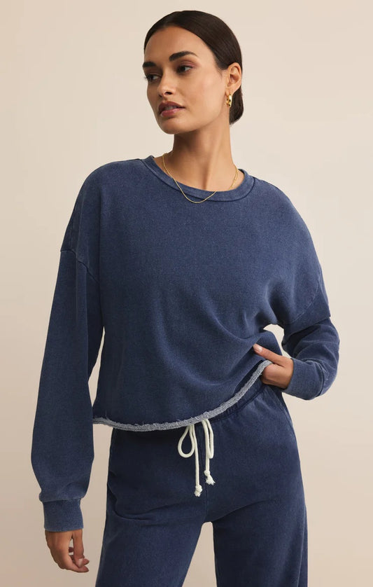 WOMEN IN BLUE SWEATSHIRT STANDING IN FRONT OF WHITE BACKGROUND