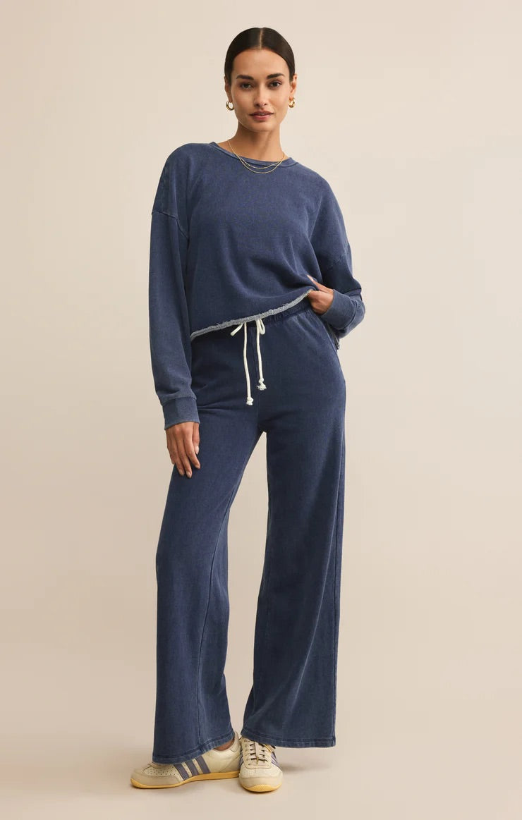 WOMEN IN BLUE SWEATSHIRT STANDING IN FRONT OF WHITE BACKGROUND