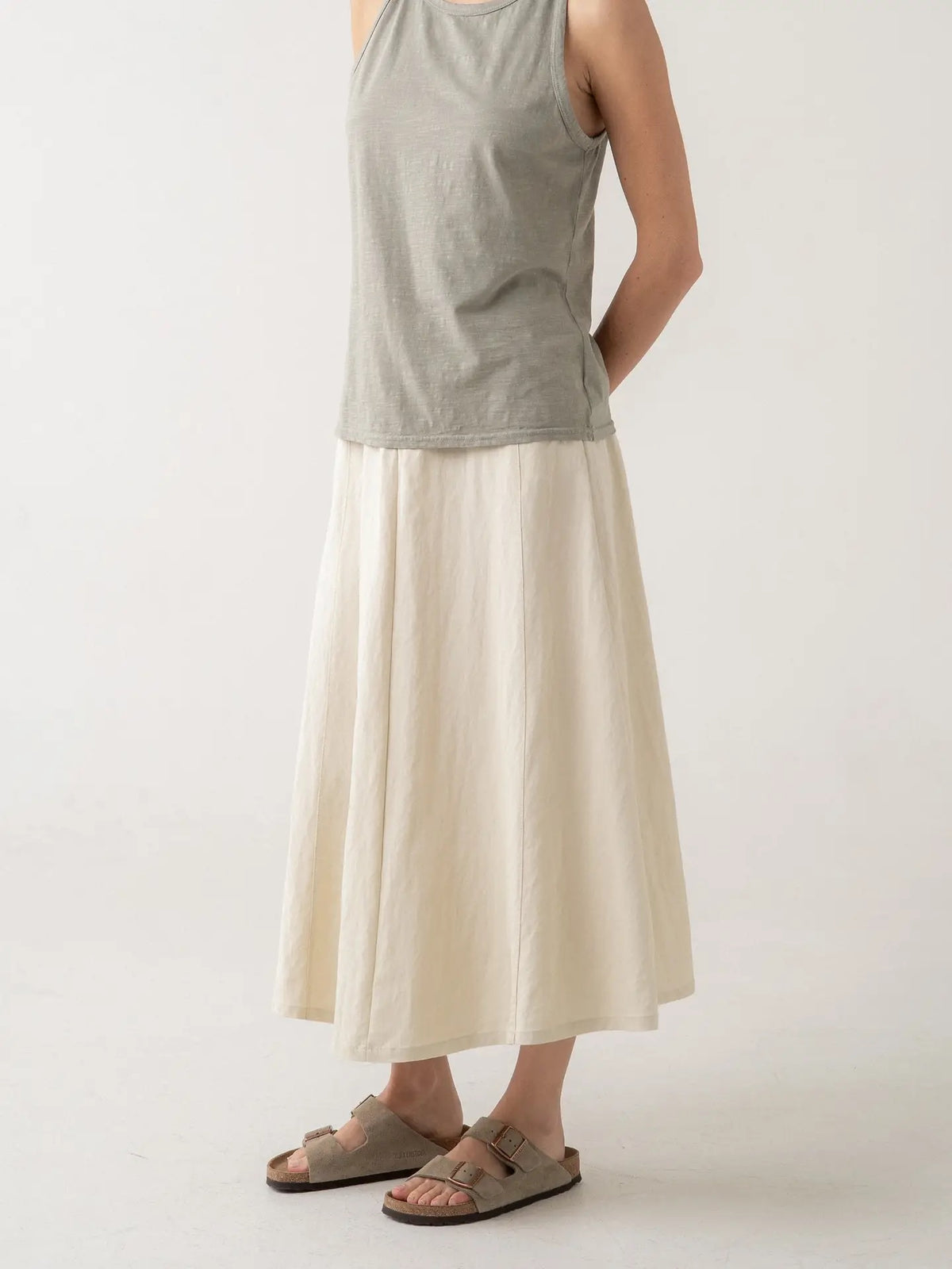 A model wearing a two-tone linen maxi skirt with a heather gray top half and an off-white bottom half, paired with taupe double-strap sandals, against a plain light gray background.