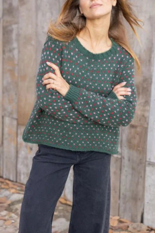 Woman wearing a green patterned sweater against a wooden wall.