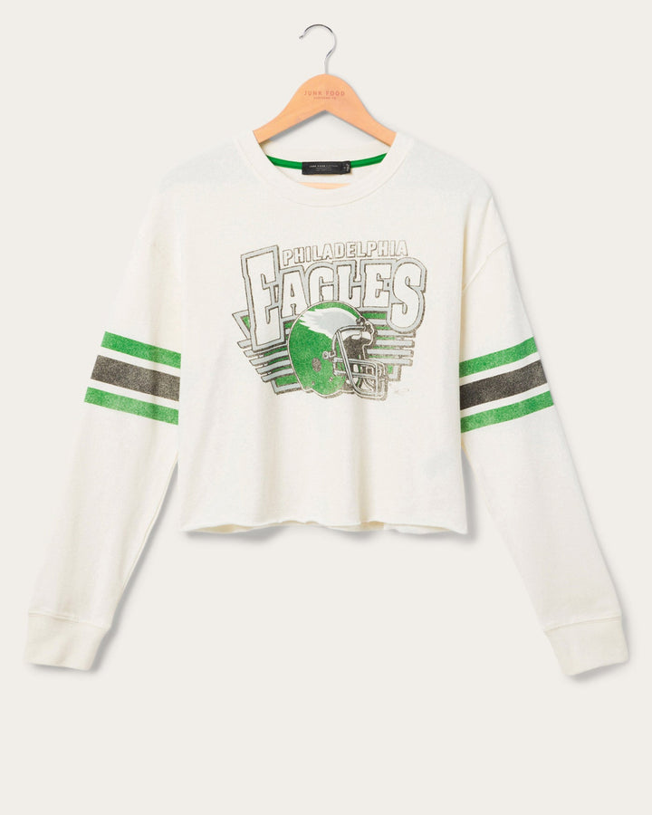 White cropped longsleeve eagles tshirt feature the football team Eagles logo with stripes on the sleeves on a hanger in front of a white background