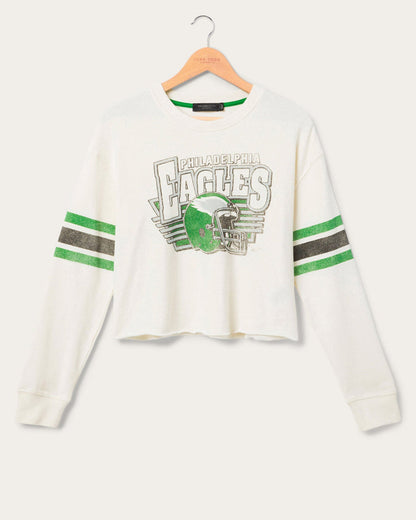 White cropped longsleeve eagles tshirt feature the football team Eagles logo with stripes on the sleeves on a hanger in front of a white background