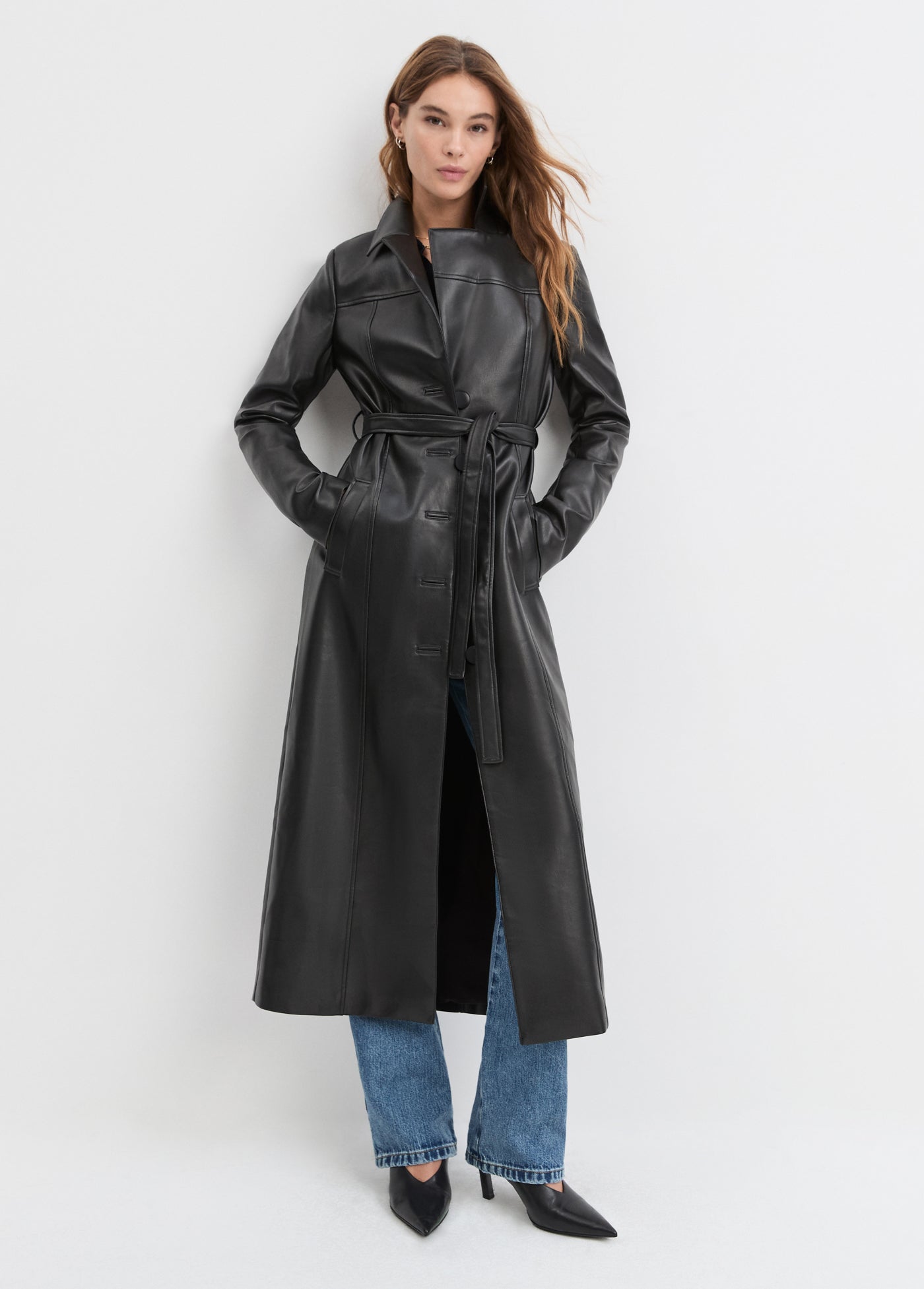 Woman wearing a black leather trench coat on a white background
