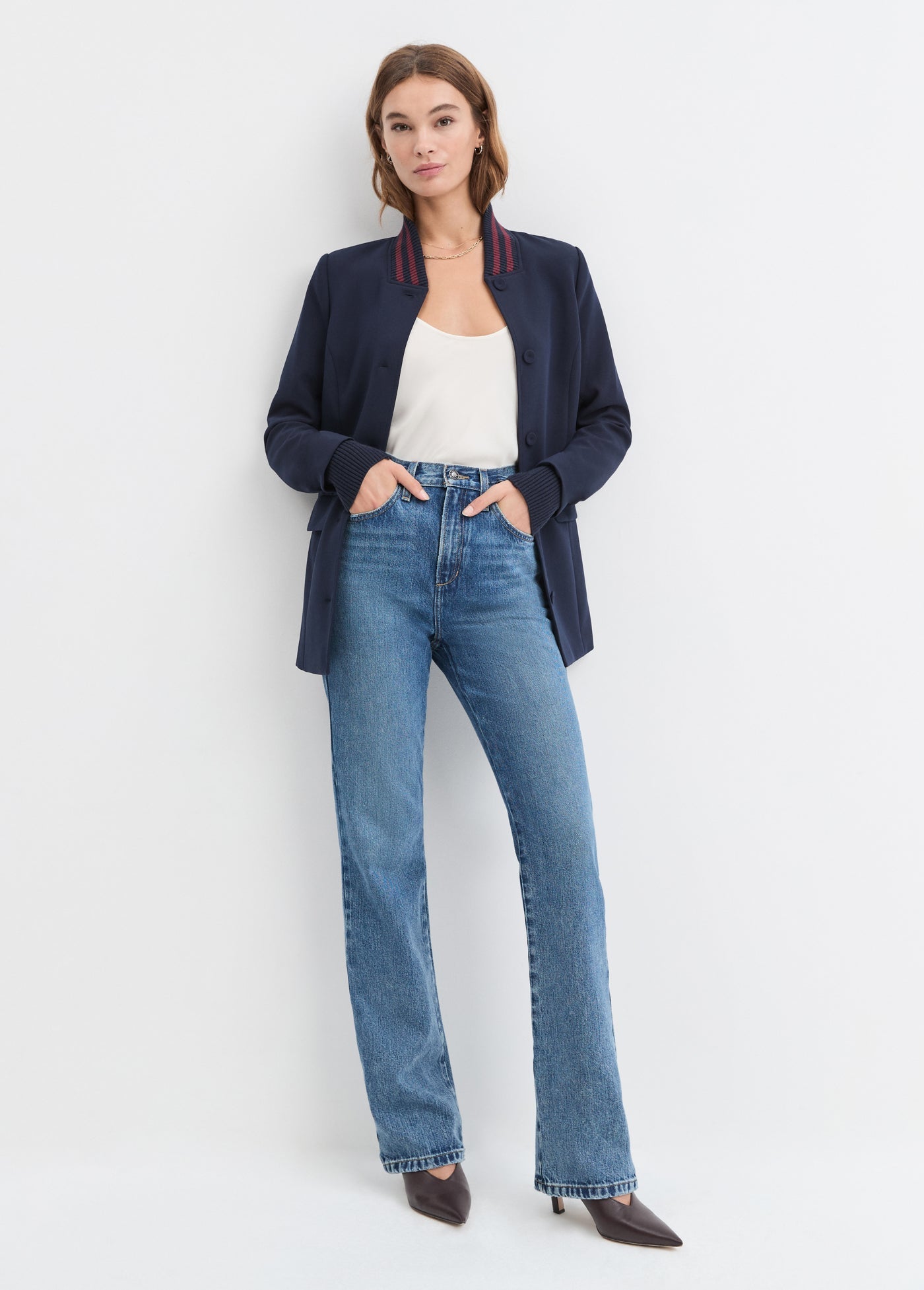 Woman wearing a navy blazer, white top, and blue jeans on a white background