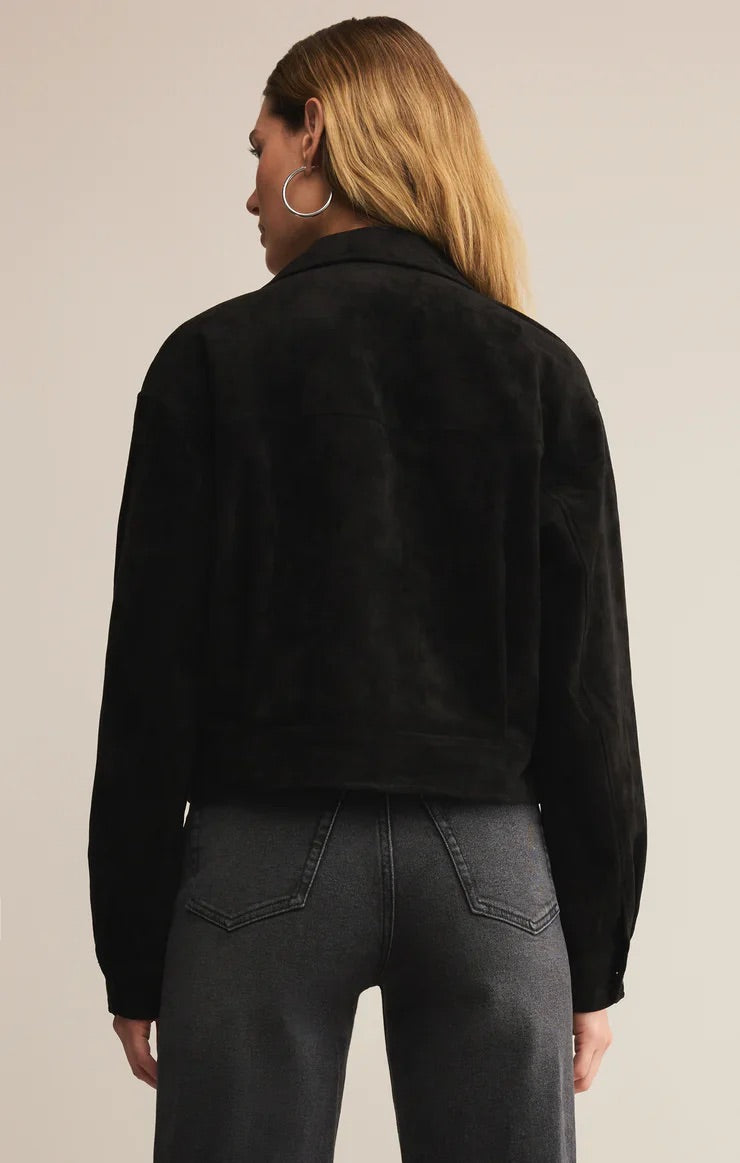 Person wearing a black jacket and dark jeans on a beige background