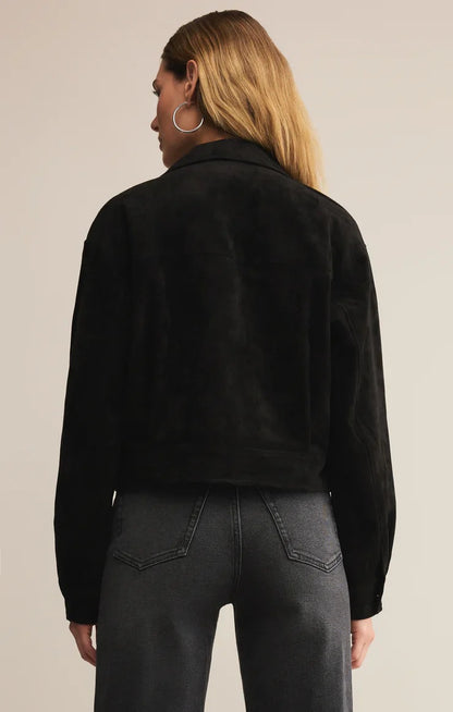 Person wearing a black jacket and dark jeans on a beige background
