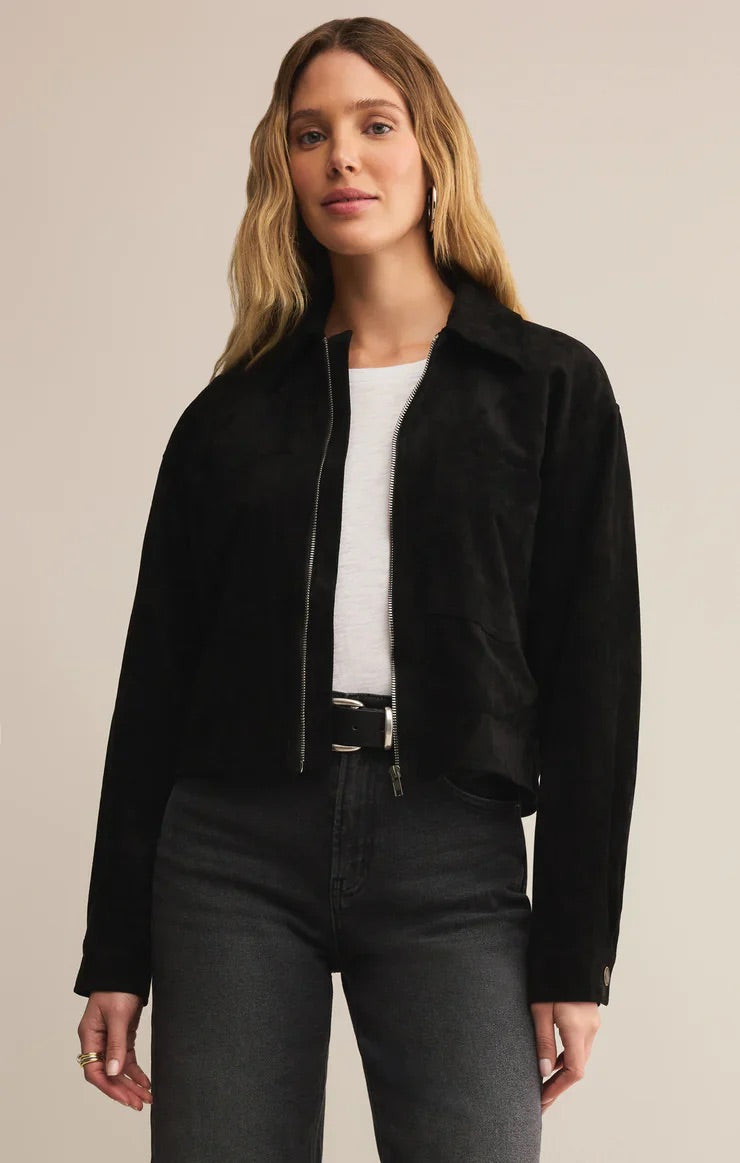 Woman wearing a black jacket over a white top and black pants on a beige background