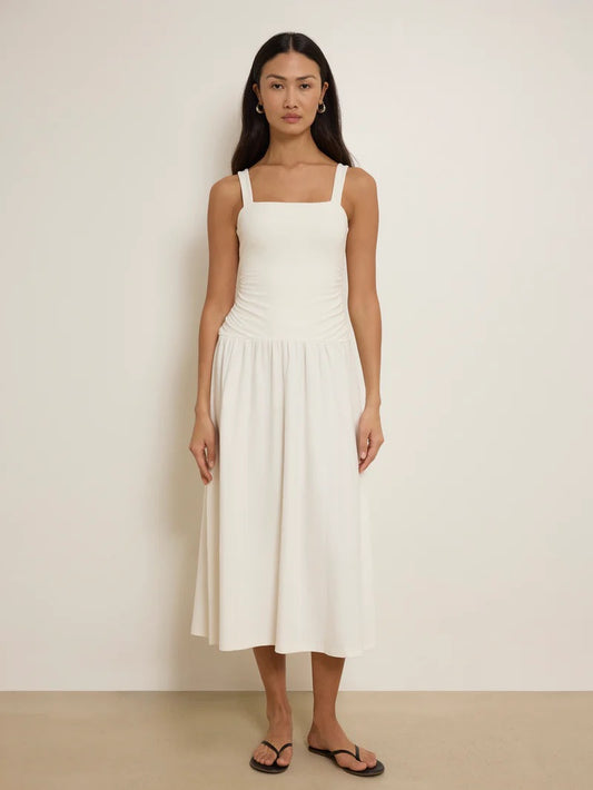 Woman wearing a white sleeveless dress against a plain background