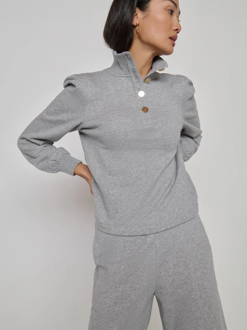 A woman modeling a light gray heathered long-sleeve mock-neck top with two decorative buttons, paired with matching gray heathered pants, against a plain light gray studio background.