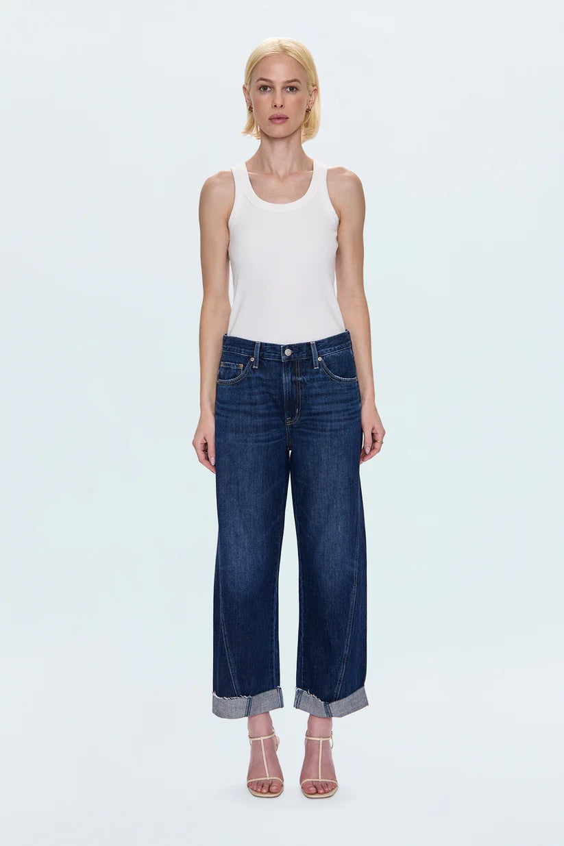 Woman wearing a white tank top and blue jeans on a light gray background