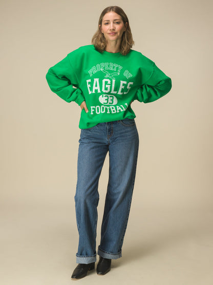 Women in front of a beige background in a green crewneck sweatshirt that says "property of eagles football"