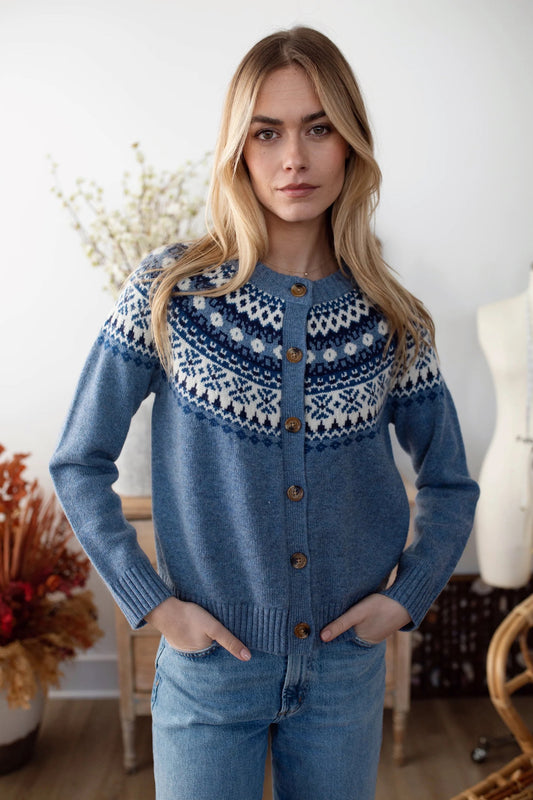 Woman wearing a blue knitted cardigan with a patterned yoke in a room setting.