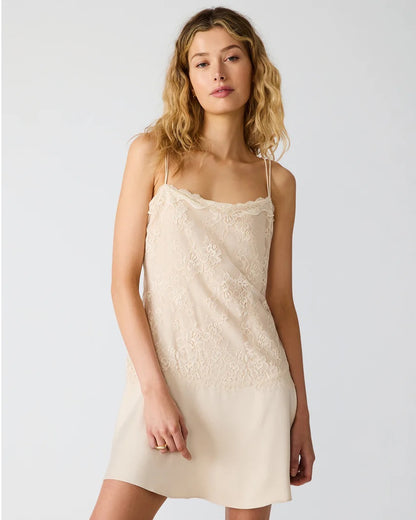 Woman wearing a beige lace slip dress against a plain background
