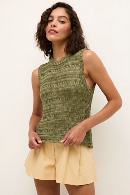 Woman wearing a green sleeveless knitted top and beige shorts on a white background