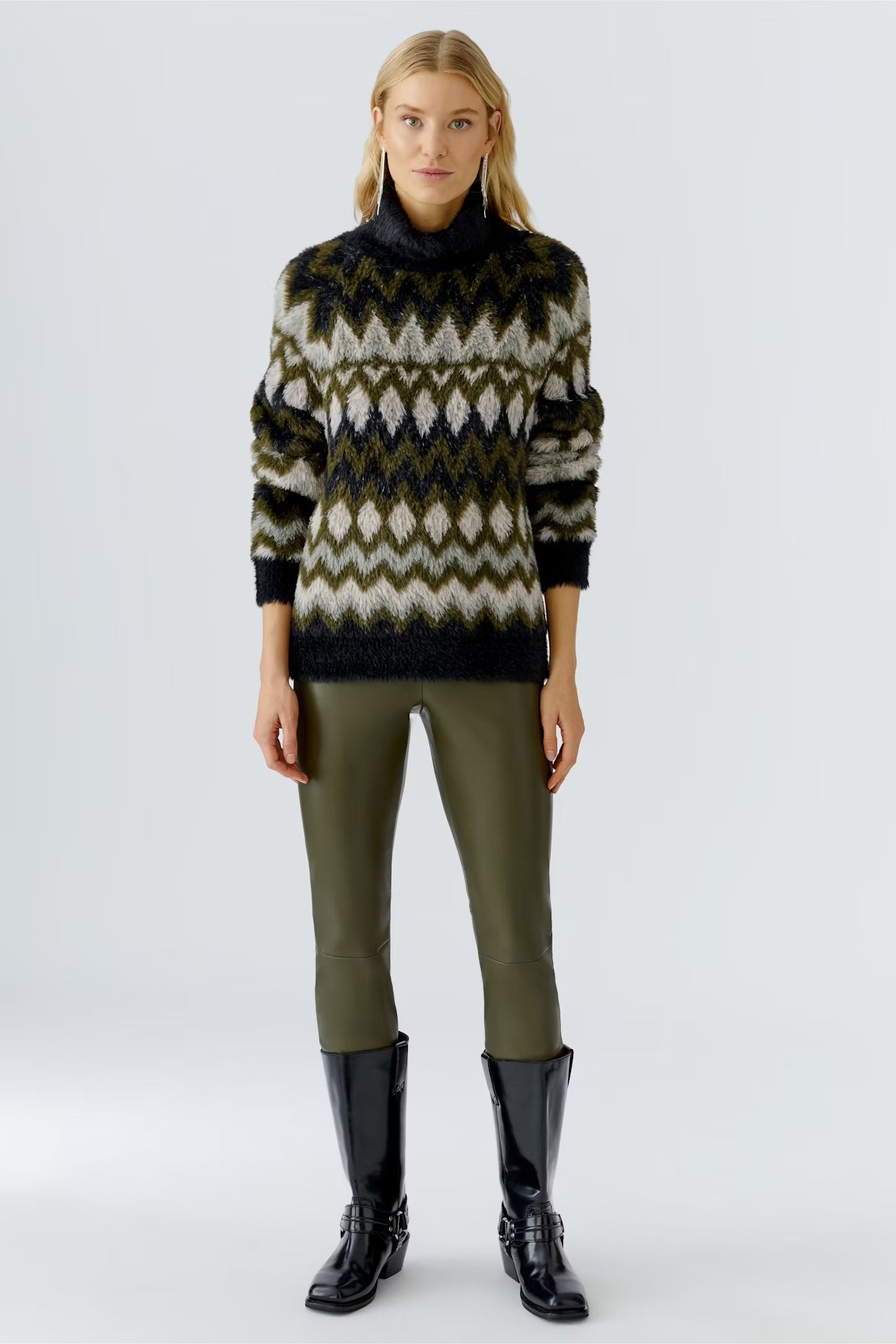 Woman wearing a patterned sweater, green pants, and black boots on a white background