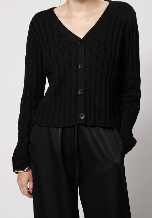 A person wearing a black ribbed knit cardigan with a V-neck and front buttons, paired with black pants, photographed against a light gray studio background.